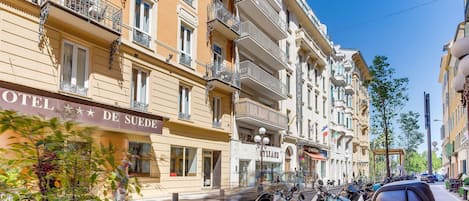 Un hotel con balcones, un cartel que dice 'HOTEL DE SUEDES' y scooters estacionados en la calle.