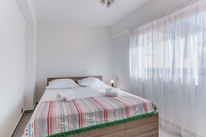 Ein ordentlich bezogenes Bett mit weißen Leinen, einer gemusterten Decke und einem hölzernen Kopfteil.
