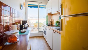 A compact kitchen with a yellow refrigerator, a coffee machine, and a dining area with a table and chairs. - PASSY AZUR AP4242 - Vue mer à 10 min de la plage (Niza)
