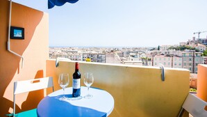 A balcony with a table set for two, a bottle of wine, and two glasses. The balcony overlooks a cityscape with buildings and a clear sky. - PASSY AZUR AP4242 - Vue mer à 10 min de la plage (Niza)