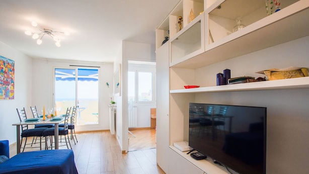 A modern living room with a flat-screen TV, dining area with chairs and a table, and a kitchen in the background. - PASSY AZUR AP4242 - Vue mer à 10 min de la plage (Niza)
