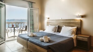 A bedroom with a large bed, a wooden headboard, and a nightstand. There is a balcony with a table and chairs, and a view of the sea. - Atlantis EDM Complex (Corfu)