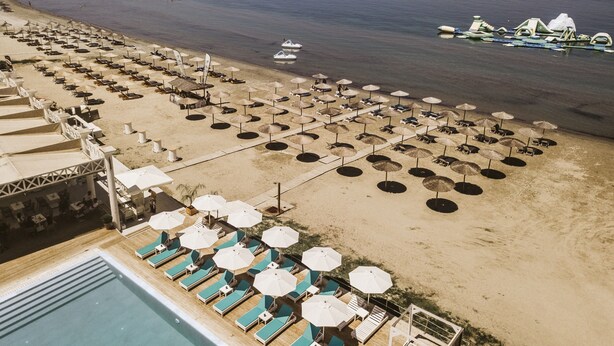 A beach resort with rows of sun loungers and umbrellas, a pool, and a pier extending into the water. - Atlantis EDM Complex (Corfu)