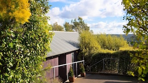 A rustic barn-style building with a metal roof, surrounded by lush greenery and a clear sky. - Dahlia Daylesford - Free WIFI walking distance to Botanic Gardens with spa bath! (Daylesford)