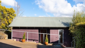 A single-story building with a corrugated metal roof, a purple exterior, and two potted plants in front. - Dahlia Daylesford - Free WIFI walking distance to Botanic Gardens with spa bath! (Daylesford)