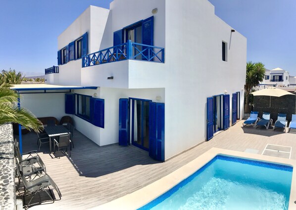 A modern two-story building with a pool, featuring blue shutters and a covered patio area. - Villa Katarina – Prime Location with Pool, AC & Spacious Outdoor Living (Playa Blanca)
