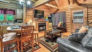 Interior acogedor de una cabaña de madera con comedor, sala de estar, chimenea y televisión.