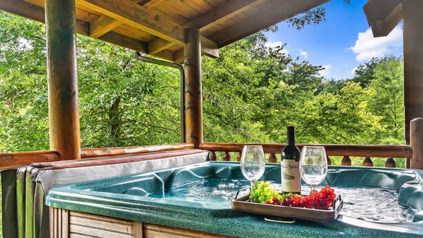 Un jacuzzi con un banco de madera, una bandeja de uvas y copas de vino.