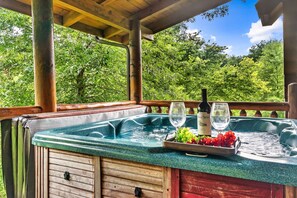 A hot tub with a wooden deck, surrounded by lush greenery. - Discount!Hot Tub, Pool & Fishing, Arcade, WiFi, Fireplace in a beautiful resort. (Sevierville)
