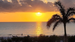 A sunset over the ocean with palm trees and beach chairs visible. - Welcome To Pleasant Paradise (Fort Myers Beach)