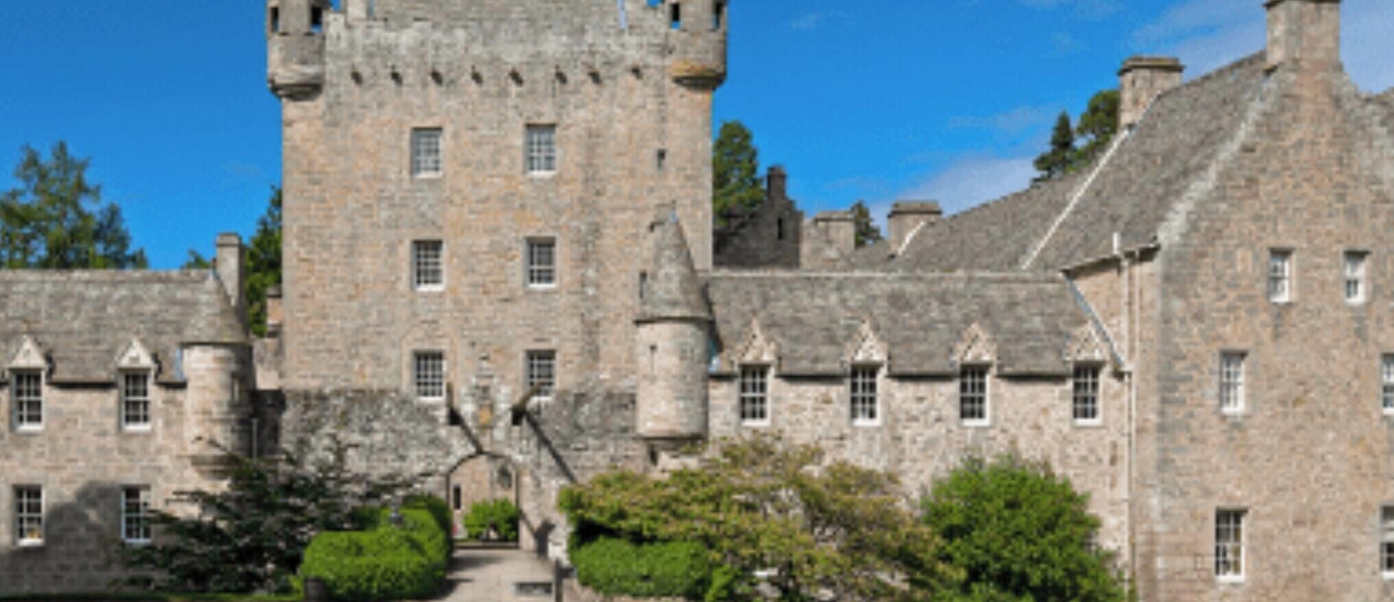 A historic stone building with multiple towers and arched windows, surrounded by greenery.