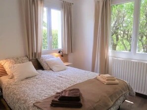 A bedroom with a bed, pillows, a nightstand, a lamp, and a window with curtains.