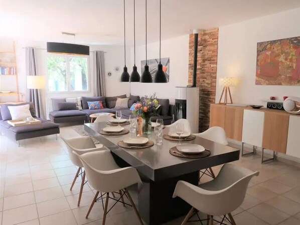 A modern living room with a dining area, featuring a sofa, a coffee table, and a dining table set for four.