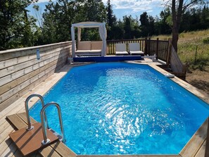 A rectangular swimming pool with a wooden deck and a canopy structure.