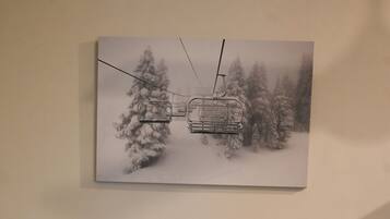 Una cama con ropa de cama estampada, dos almohadas y un cuadro en la pared de un telesilla en un bosque nevado.