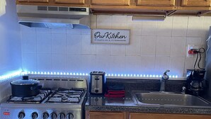 Ett kök med träskåp, en spis i rostfritt stål, en brödrost och LED-lampor längs bänkskivan.