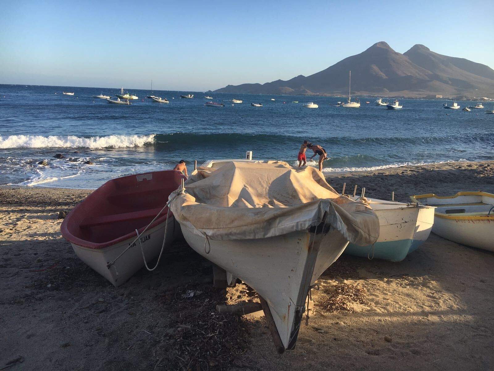 Una playa con varios barcos anclados en la arena, una montaña al fondo y un cielo despejado.
