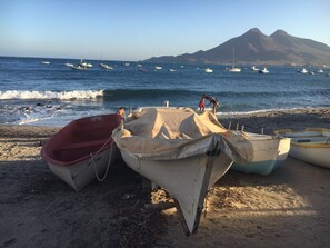 A beach with several boats anchored on the sand, a mountain in the background, and a clear sky.