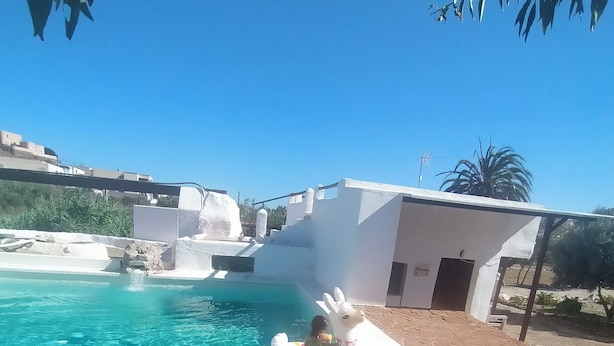 A clear blue pool with a child in a float, surrounded by white buildings and a palm tree. - WINTER LONG STAY.  OASIS IN CABO DE GATA (El Pozo de los Frailes)