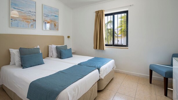 Habitación de hotel con dos camas, un escritorio, una ventana con cortinas y una obra de arte en la pared.