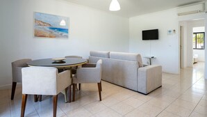Una sala de estar moderna con una mesa de comedor redonda, un sofá gris y un cuadro con una playa.