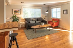 Uma sala de estar moderna com um sofá cinzento, uma poltrona vermelha, uma mesa de centro de madeira e uma mesinha lateral com uma luminária.