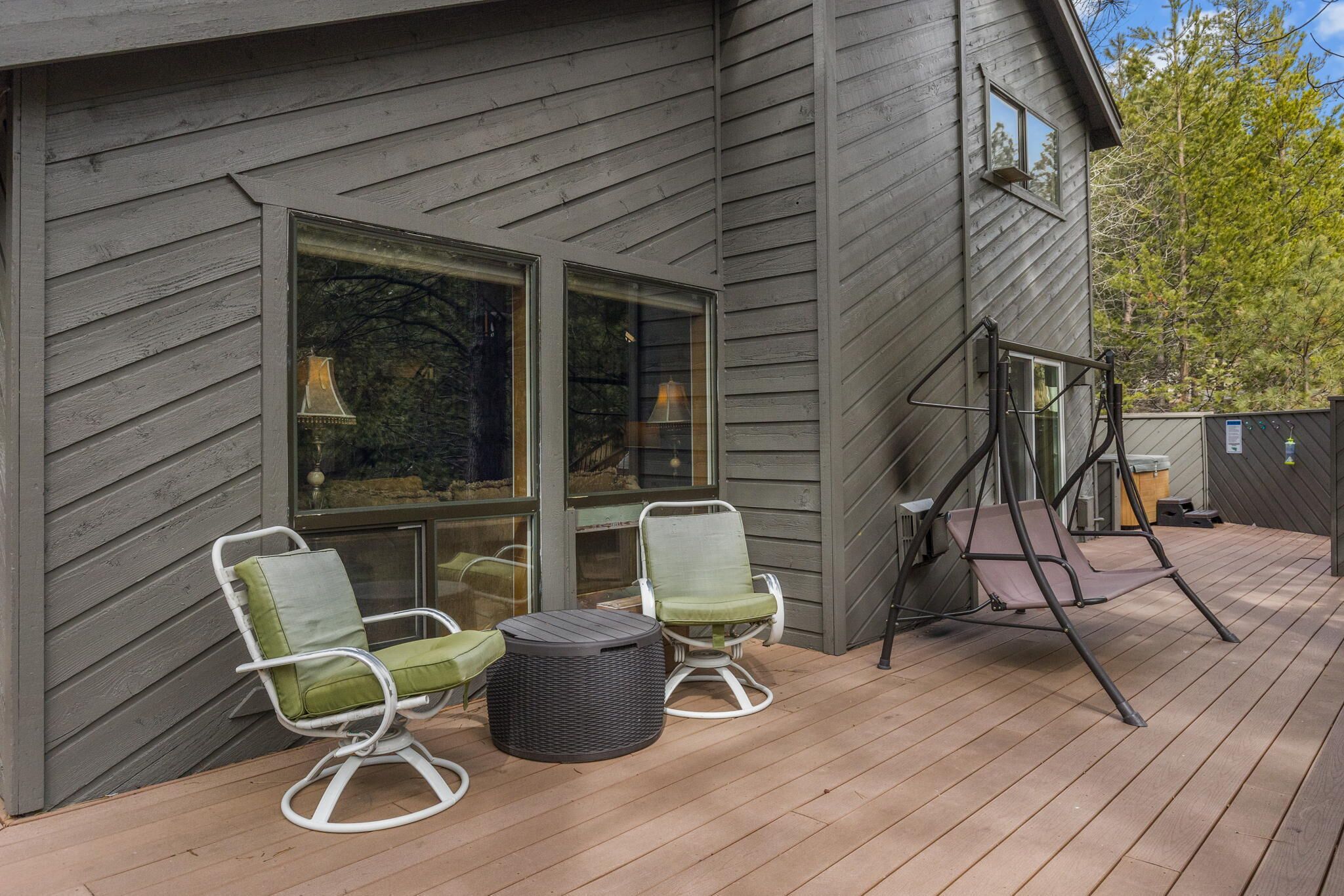 A deck with two rocking chairs and a small table, adjacent to a house with large windows and a swing set.