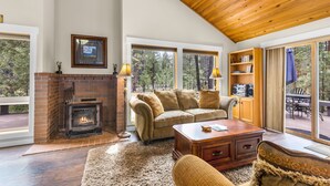 A cozy living room with a fireplace, a sofa, a coffee table, and a bookshelf. - Private Hot Tub ~ In the heart of Sunriver ~ SHARC Passes~Fireplace~Sleeps 10 (Sunriver)