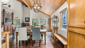 A dining area with a wooden ceiling, a chandelier, and a view of the outdoors through large windows. - Private Hot Tub ~ In the heart of Sunriver ~ SHARC Passes~Fireplace~Sleeps 10 (Sunriver)