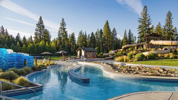 A swimming pool with a curved design, surrounded by a grassy area and trees. - Private Hot Tub ~ In the heart of Sunriver ~ SHARC Passes~Fireplace~Sleeps 10 (Sunriver)