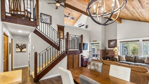 A spacious living area with a wooden staircase, a dining table, and a cozy seating arrangement. - Private Hot Tub ~ In the heart of Sunriver ~ SHARC Passes~Fireplace~Sleeps 10 (Sunriver)