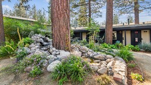 A rustic lodge with a stone waterfall, surrounded by lush greenery and tall trees. - South Lake Chalet #2 (South Lake Tahoe)