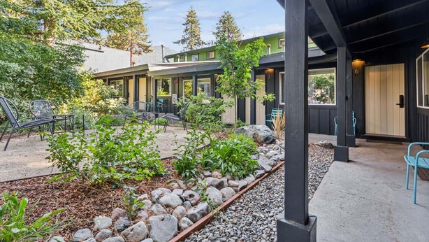 A covered outdoor area with seating, a garden with rocks and plants, and a building with multiple windows and doors. - South Lake Chalet #2 (South Lake Tahoe)