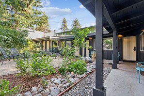 A covered outdoor area with seating, a garden with rocks and plants, and a building with multiple windows and doors. - South Lake Chalet #2 (South Lake Tahoe)