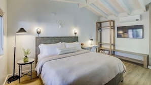 A bedroom with a bed, bedside tables, a floor lamp, a wall-mounted TV, and a wooden bench. - South Lake Chalet #2 (South Lake Tahoe)