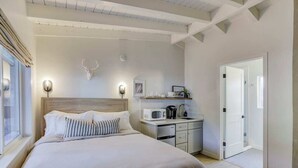 Un dormitorio con una cama grande, una mesita de noche con microondas, un mueble pequeño y una puerta que da a otra habitación.