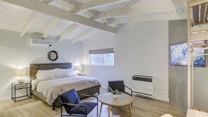 A bedroom with a bed, bedside tables, a round table, two chairs, a radiator, and a TV on the wall.