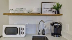 A compact kitchen with a white microwave, a coffee maker, and a sink.