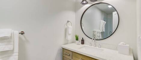 Um banheiro moderno com toucador branco, espelho redondo e três luminárias no teto.