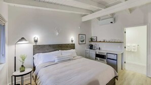A modern bedroom with a large bed, bedside table, lamp, and a kitchenette area. - South Lake Chalet #8 (South Lake Tahoe)