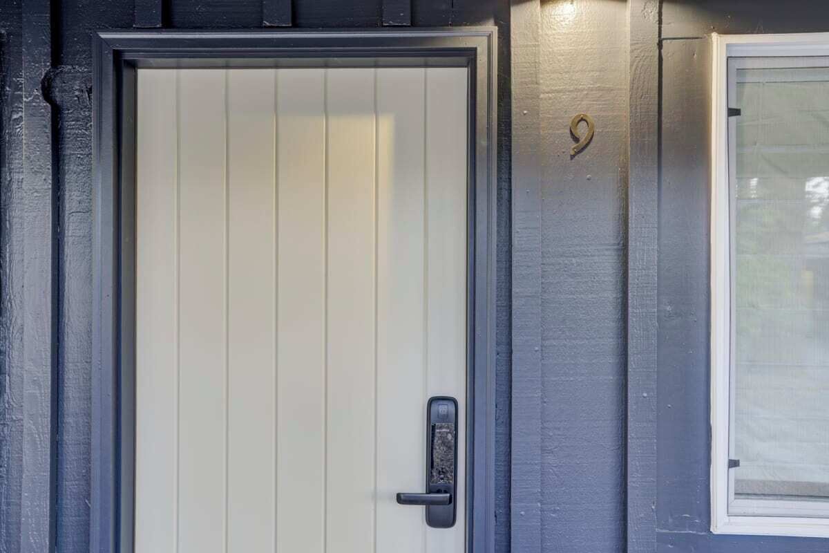 A door with a vertical panel design and a modern handle, adjacent to a window with a white frame.