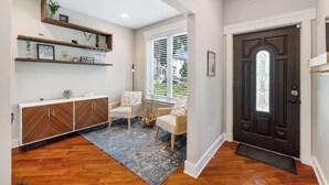 Uma entrada moderna com uma porta de madeira escura, um console branco, duas cadeiras de vime e um tapete azul.