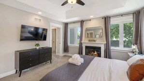 Um quarto com cama, TV, lareira e ventoinha no teto.