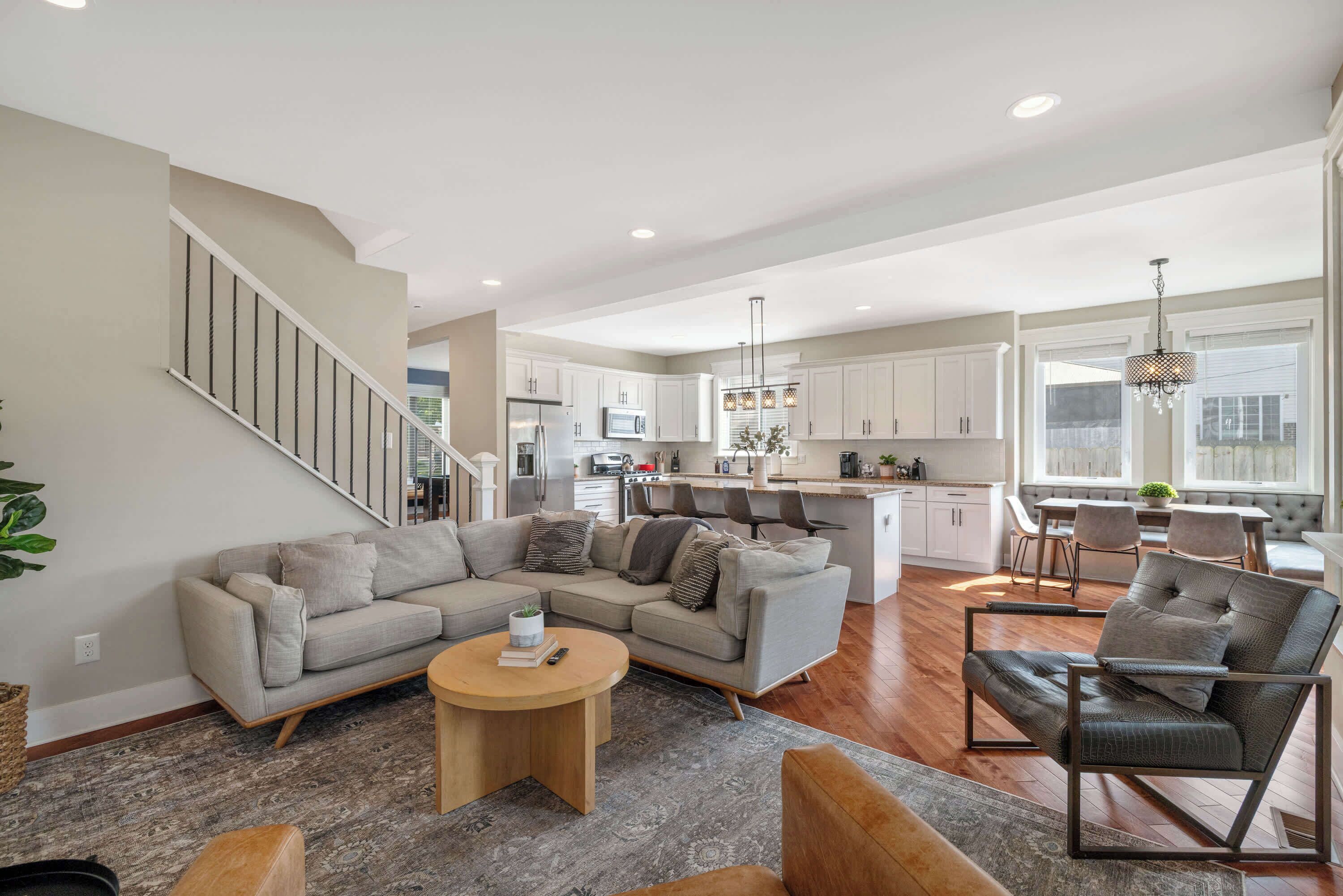 A spacious living area with a sofa, coffee table, and a chair. A kitchen with white cabinets and a dining area with a table and chairs are visible.