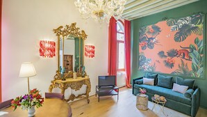 Een woonkamer met een grote spiegel, een kroonluchter, een bank en een wand met tropisch thema.