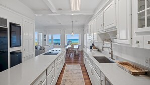 Une cuisine spacieuse avec des meubles blancs, un grand îlot central et une vue sur l’océan.