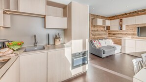 A modern kitchen with built-in appliances, a dining area with a grey sofa, and a wooden accent wall. - 100m from ski slopes, 5th floor, view lake/mountain, tv, ski locker, 35m², Tignes (Tignes)