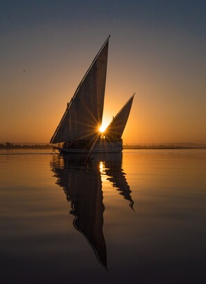 A sailboat with its sails fully extended, reflecting on calm water during sunset.