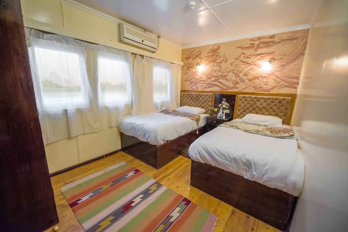 A hotel room with two beds, a wooden floor, a colorful striped rug, and a decorative wall mural.