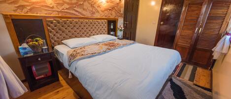 A bedroom with a large bed, a wooden headboard, a nightstand with a lamp, and a door with louvered shutters.
